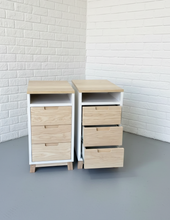 Load image into Gallery viewer, Two wooden nightstands with drawers against a white brick wall.
