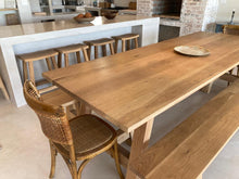 Load image into Gallery viewer, A trestle-style dining table made of rustic oak with A-shaped legs, accompanied by matching benches and wooden chairs, set in a kitchen-dining area with exposed brick walls.