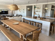 Load image into Gallery viewer, A trestle-style dining table made of rustic oak with A-shaped legs, accompanied by matching benches and wooden chairs, set in a kitchen-dining area with exposed brick walls.