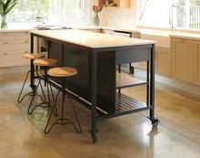 Load image into Gallery viewer, A dark grey metal kitchen island with a white quartz stone top, two drawers, and oak shelving. It has industrial castors and is displayed in a kitchen setting with stools in front of it.