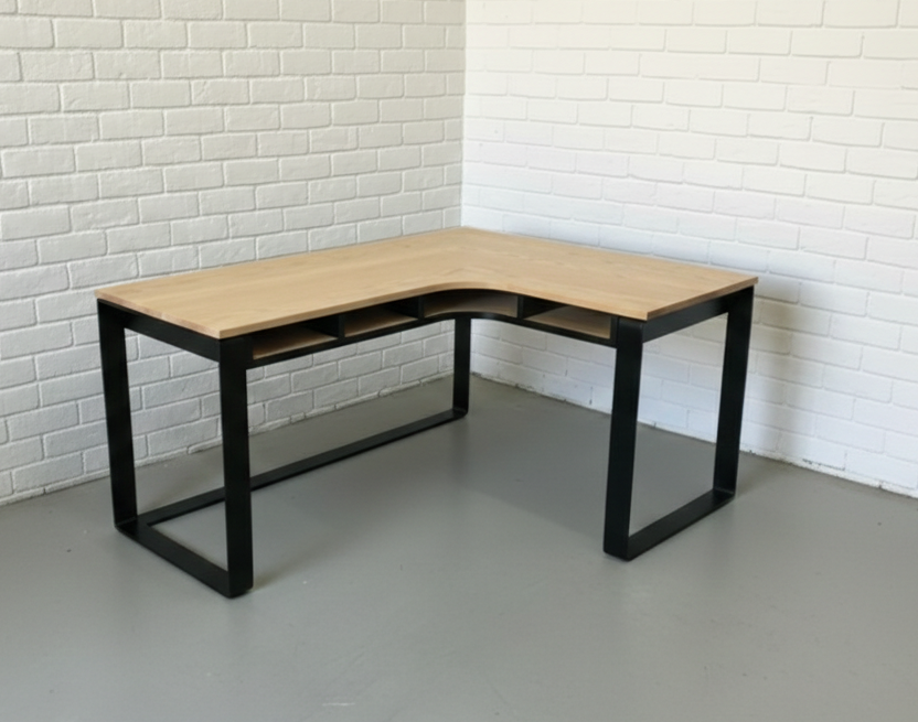 The Kiki L-Shape Desk features a solid Ash timber top on a matte black flat-bar steel frame with under-desk cubbies. Custom made to order in South Africa.