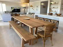 Load image into Gallery viewer, A trestle-style dining table made of rustic oak with A-shaped legs, accompanied by matching benches and wooden chairs, set in a kitchen-dining area with exposed brick walls.
