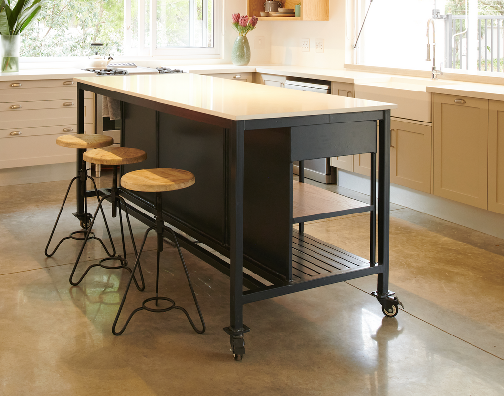 The Serengeti Steel Island features a dark powder-coated frame, solid Oak shelving, stone quartz top, and industrial castors. Designed and made in SA.