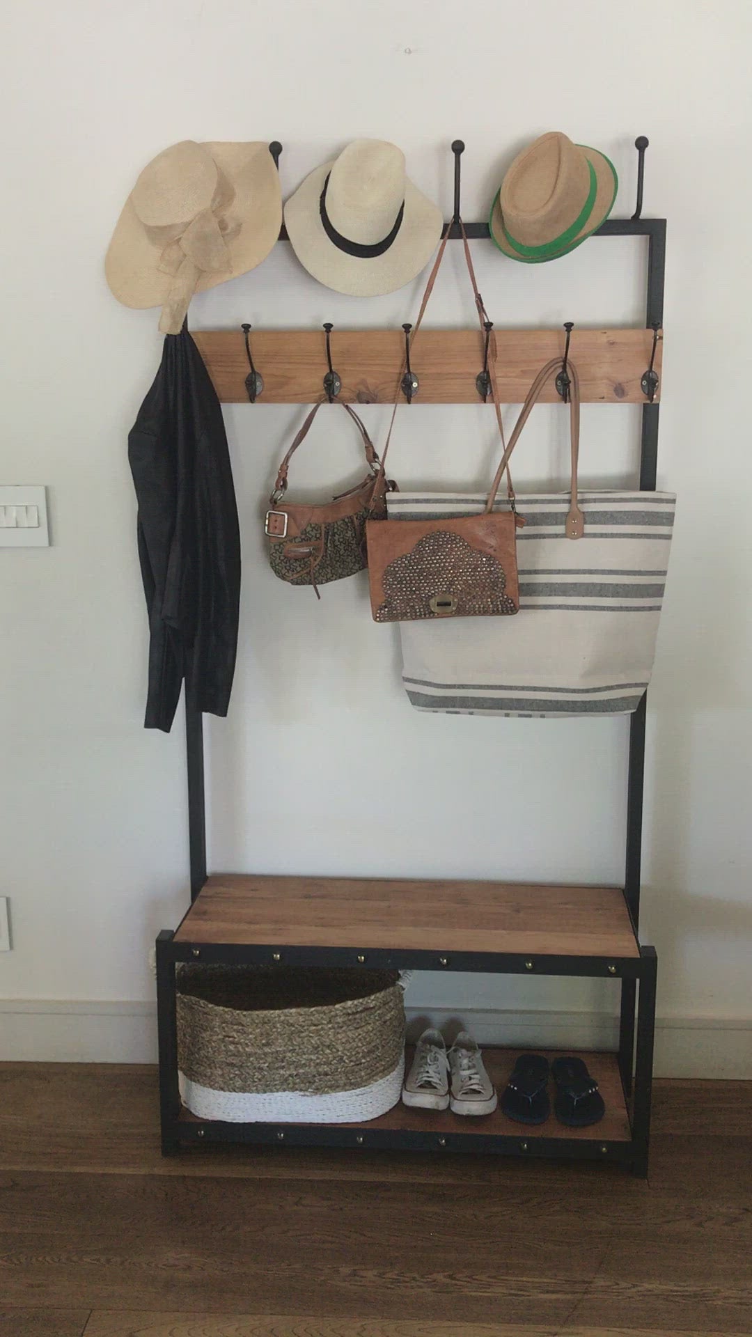 A black metal coat stand with a wooden shelf below, holding various items including hats, bags, and shoes.