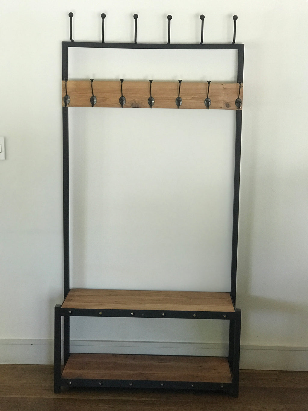 A black metal coat stand with a wooden shelf below, holding various items including hats, bags, and shoes.