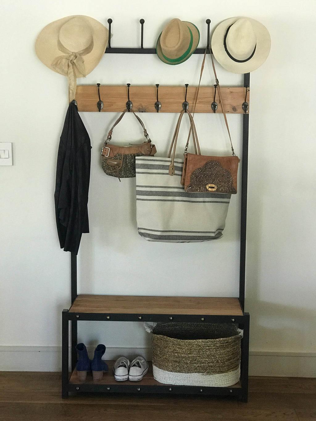 A black metal coat stand with a wooden shelf below, holding various items including hats, bags, and shoes.