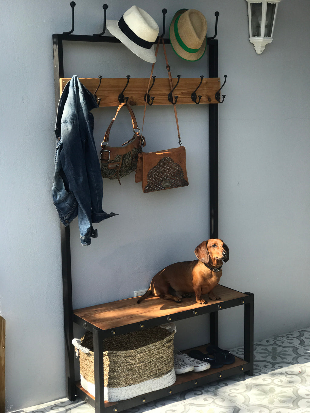 A black metal coat stand with a wooden shelf below, holding various items including hats, bags, and shoes.