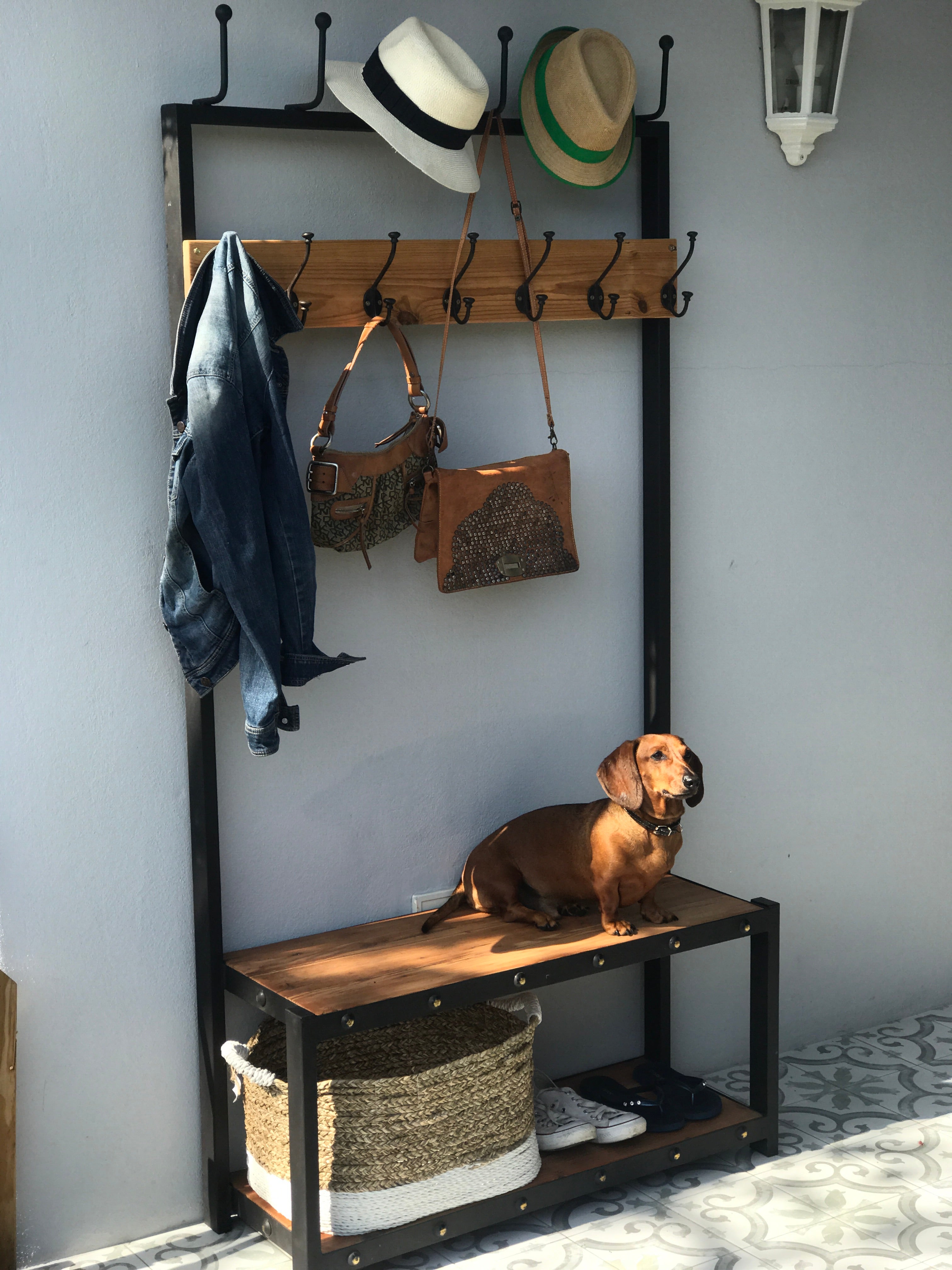 A black metal coat stand with a wooden shelf below, holding various items including hats, bags, and shoes.