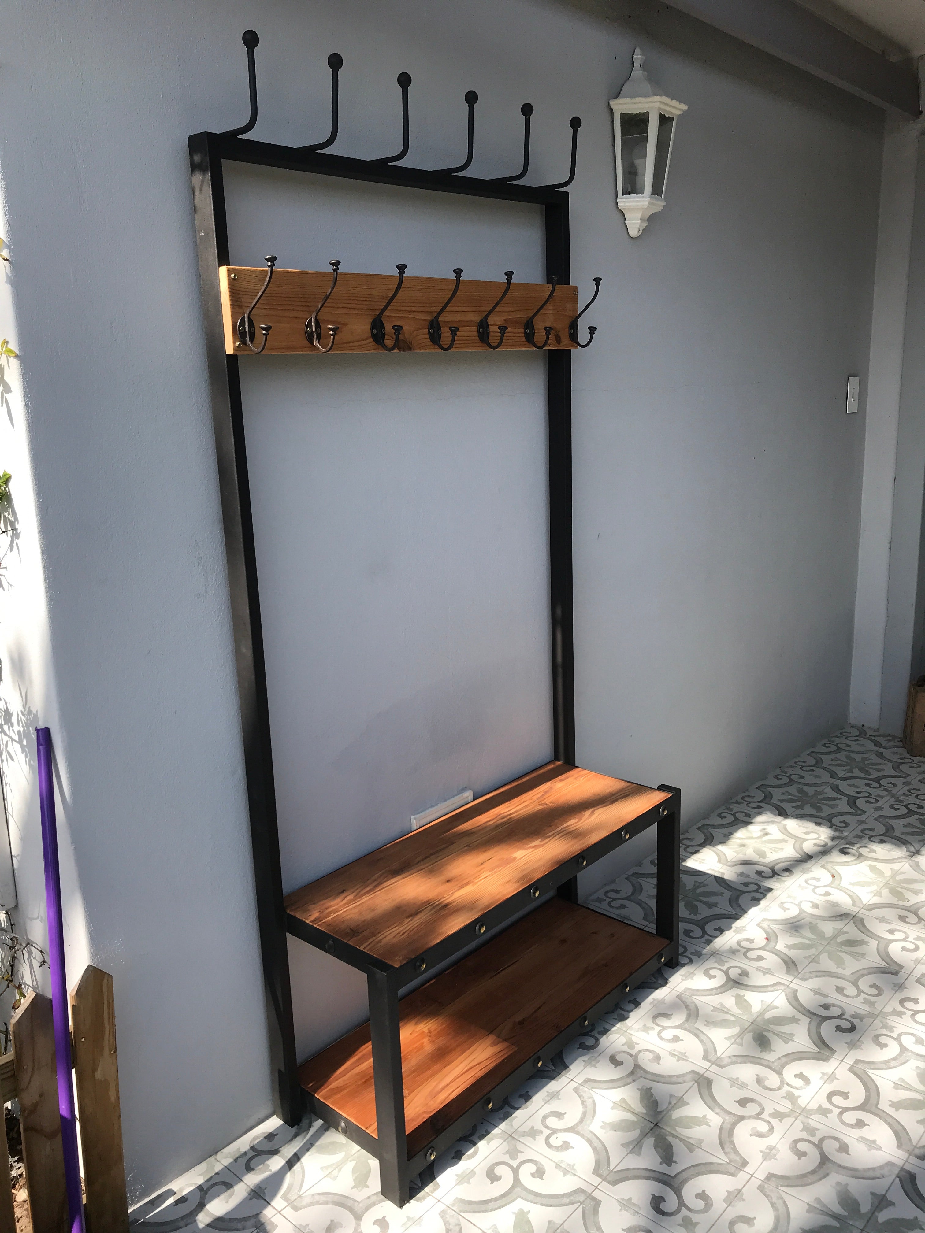 A black metal coat stand with a wooden shelf below, holding various items including hats, bags, and shoes.