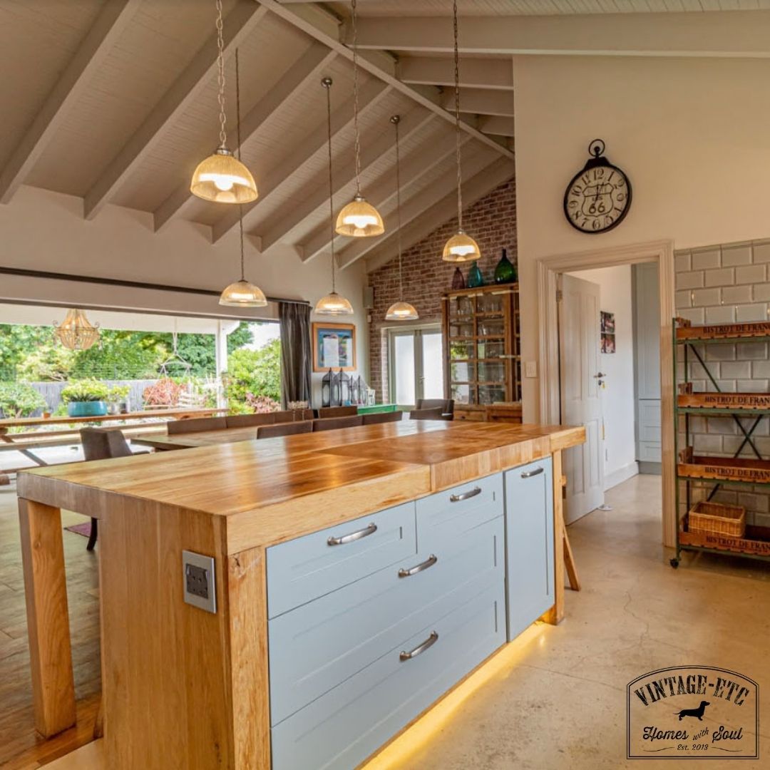 Modern style kitchen with a solid oak sharing island, under-counter LED lighting, and a butcher's block countertop. The island is accompanied by a gray cabinet with a wood countertop and a hanging pendant lamp.